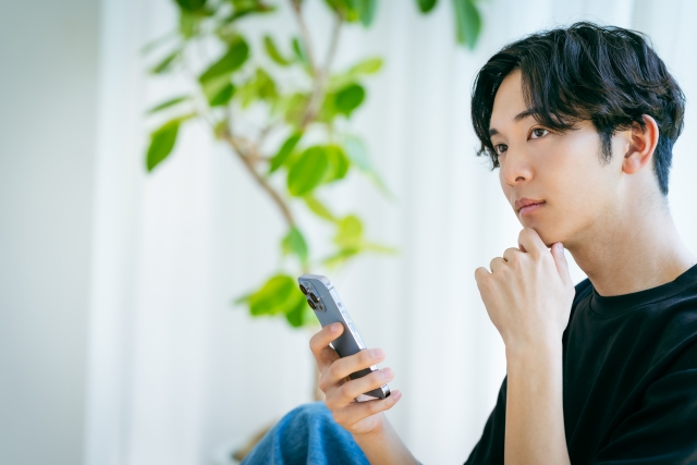 スマホを弄りながら考える男性